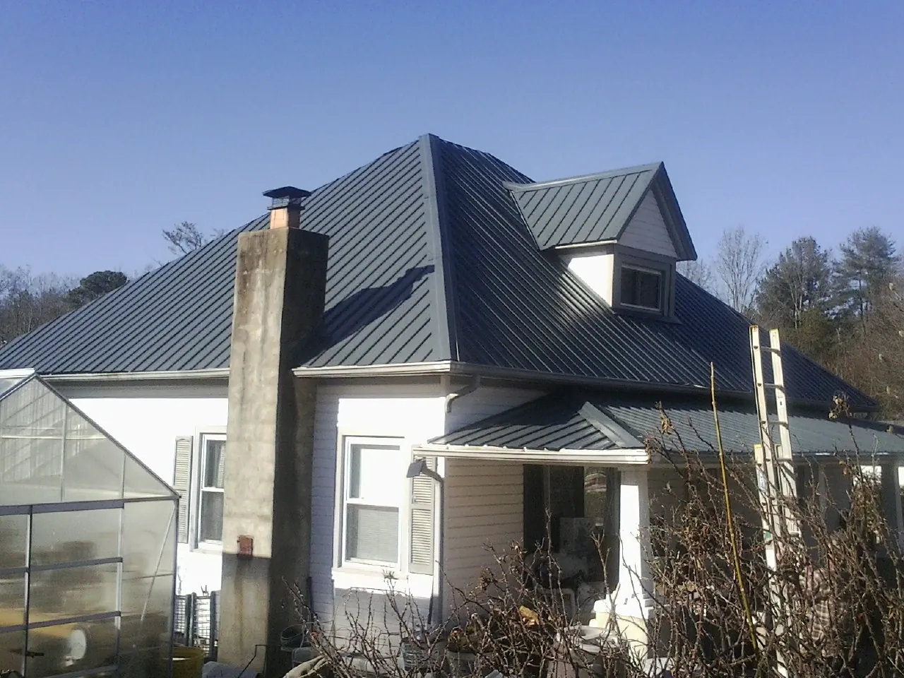Dark blue standing seam metal roof on a white farmhouse with dormer — Slate & Tile Roof Repair by Roofing Brothers in Poneto