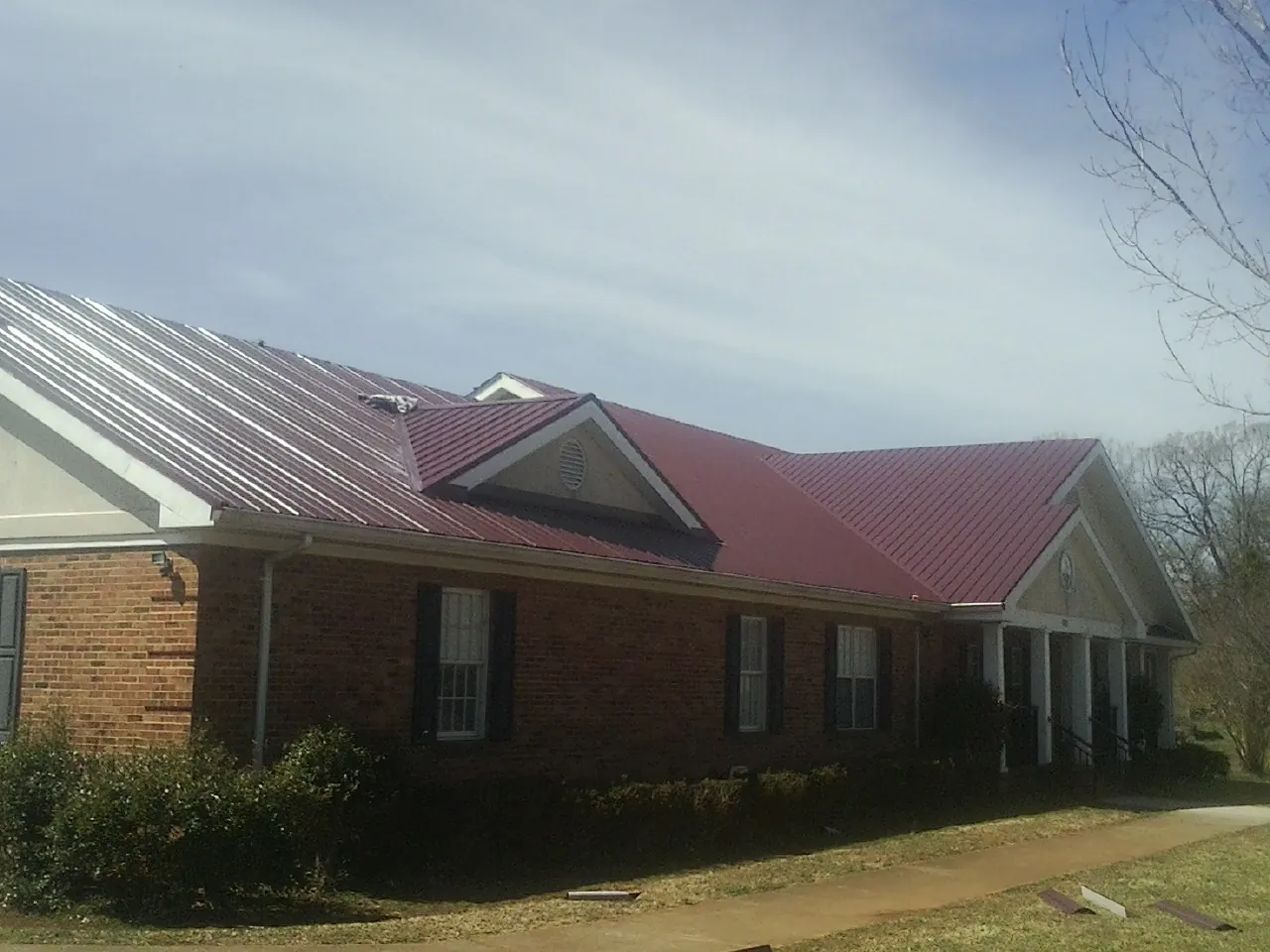 Red metal roof with gabled entries on a long brick building, from a Hail Damage Roof Repair job in Poneto