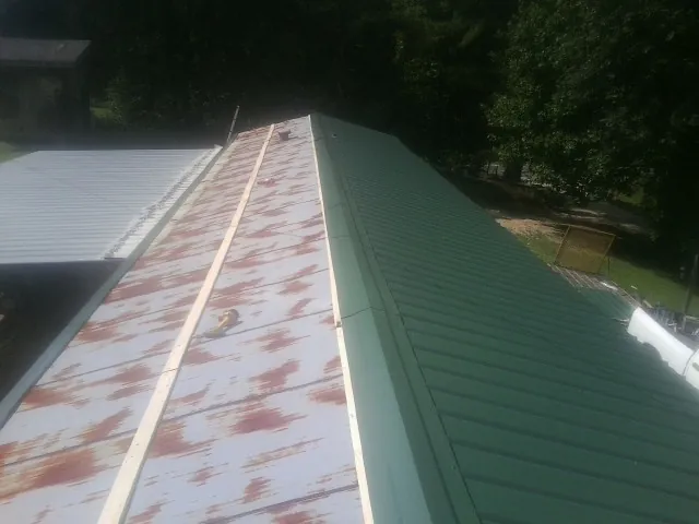 Old rusted panels beside newly installed green metal roofing — Wind Damage Roof Repair by Roofing Brothers in Poneto