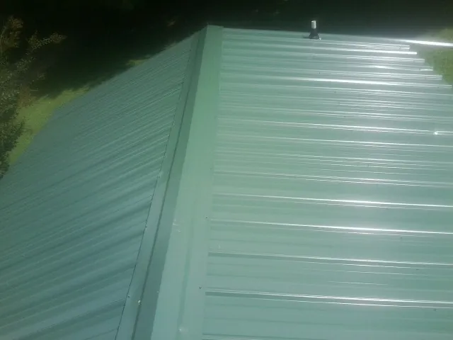 New green metal panels meeting at the ridge of a roof — Flat Roof Repair work by our crew in Poneto