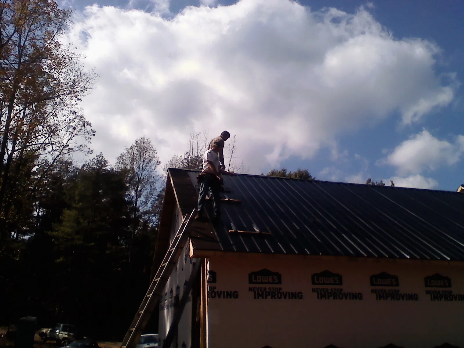 Roofer fastening dark metal panels high against a cloudy sky, from a Roof Inspection job in Poneto