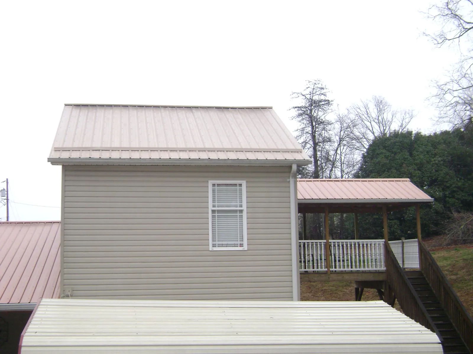 Tan metal roofs on a two story addition and attached porch, from a Roof Replacement job in Poneto